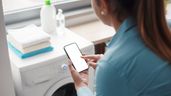 Mujer revisando teléfono delante de una lavadora