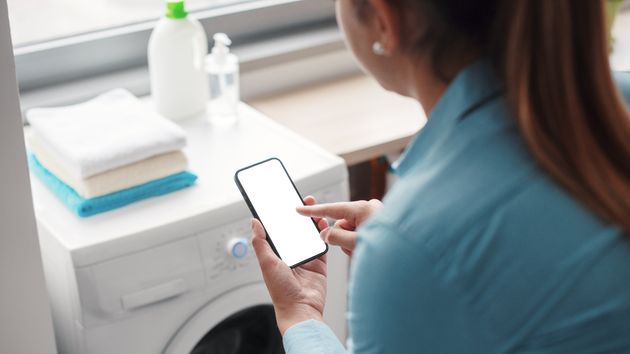 Mujer revisando teléfono delante de una lavadora