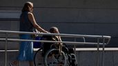 Una persona ayudando a una mujer mayor en silla de ruedas