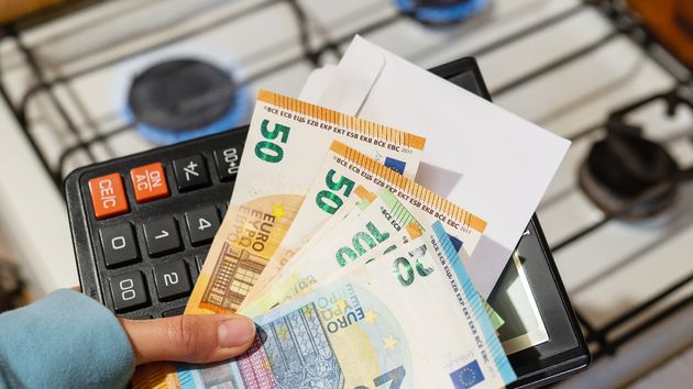Una persona sujetando una factura con billetes de euro con el gas encendido